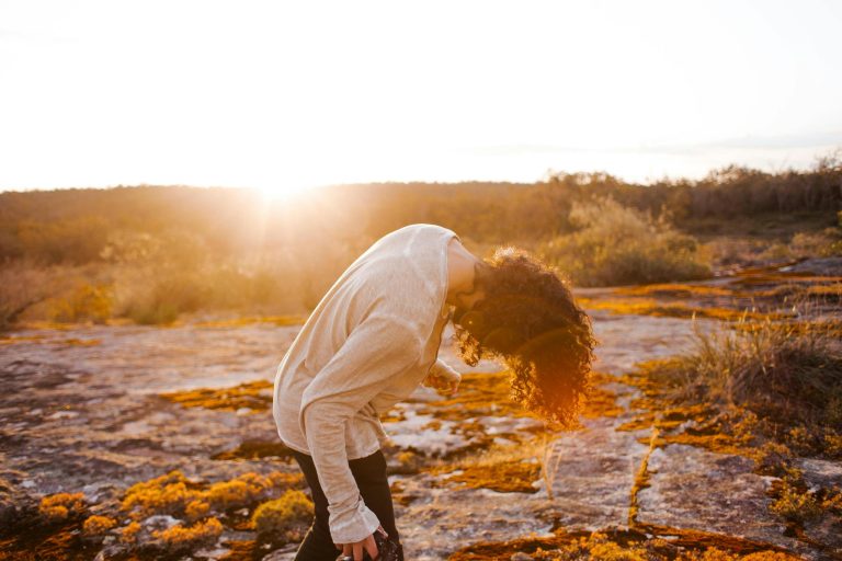 A person bending forward in a sunlit landscape, capturing nature's warm glow.