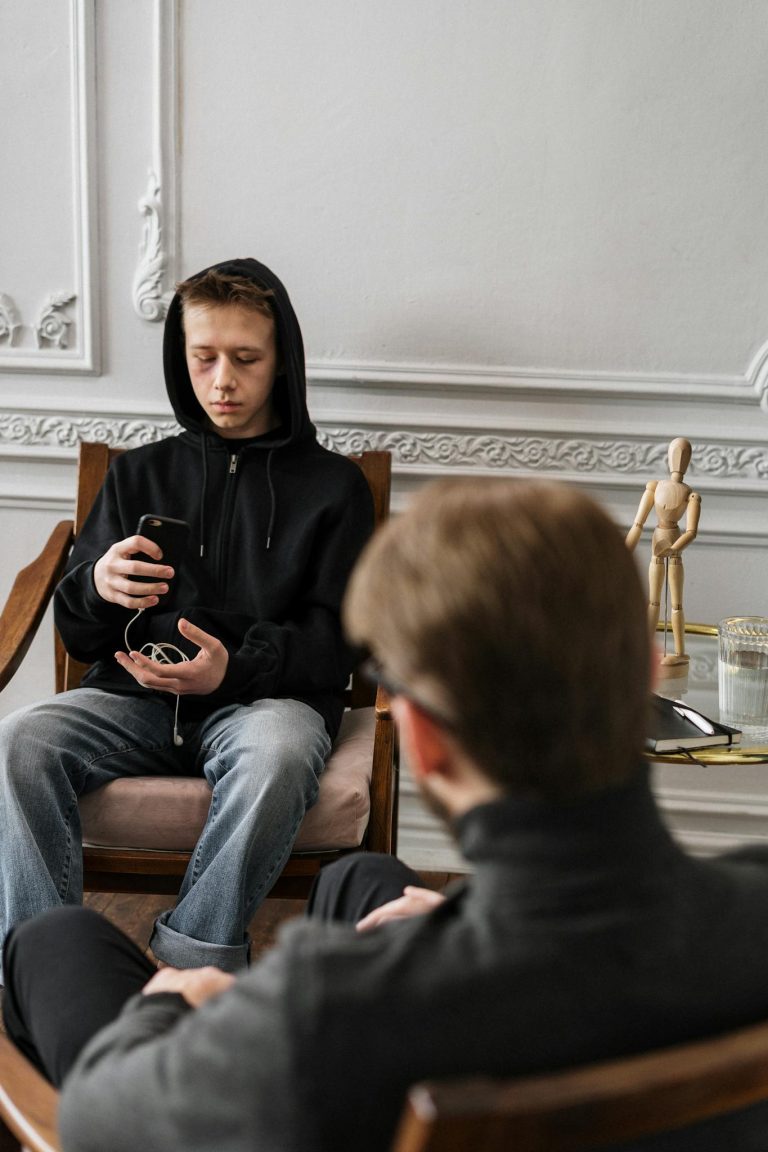 A teenage boy in a black hoodie during a therapy session, using his phone.